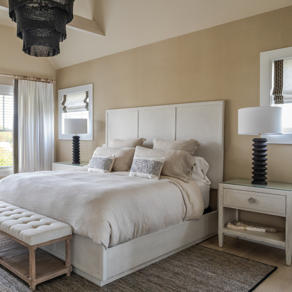Neatly made bed in a bedroom with beige walls, a nightstand, and a lamp.