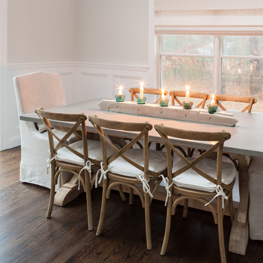 Dining room with wooden table and chairs, candles on the table, and a window in the background.