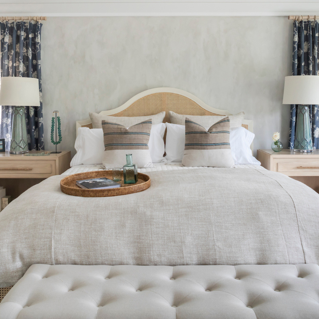 Neatly made bed with decorative pillows and a tray on a neutral-toned headboard.