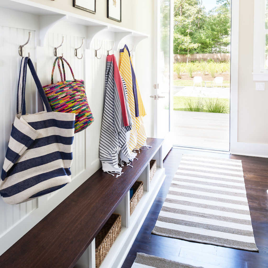 Entryway with coat hooks, bench, and colorful bags.
