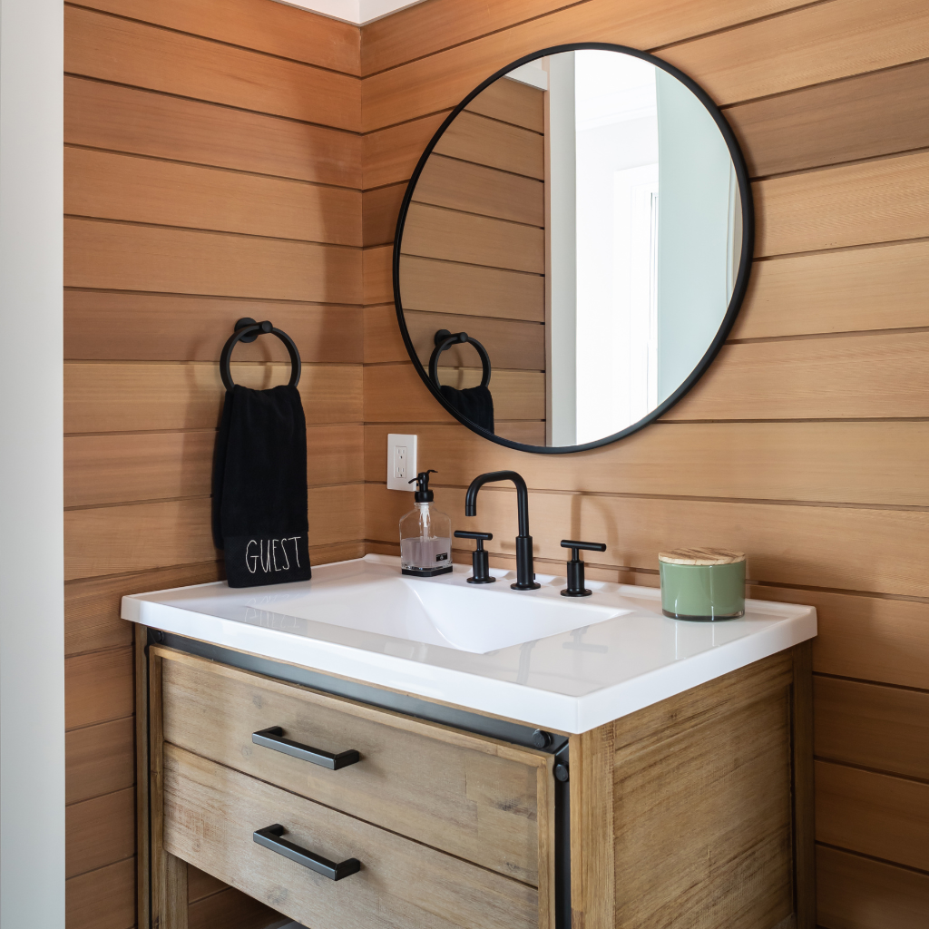 Bathroom vanity with round mirror, black faucet, and wooden walls.