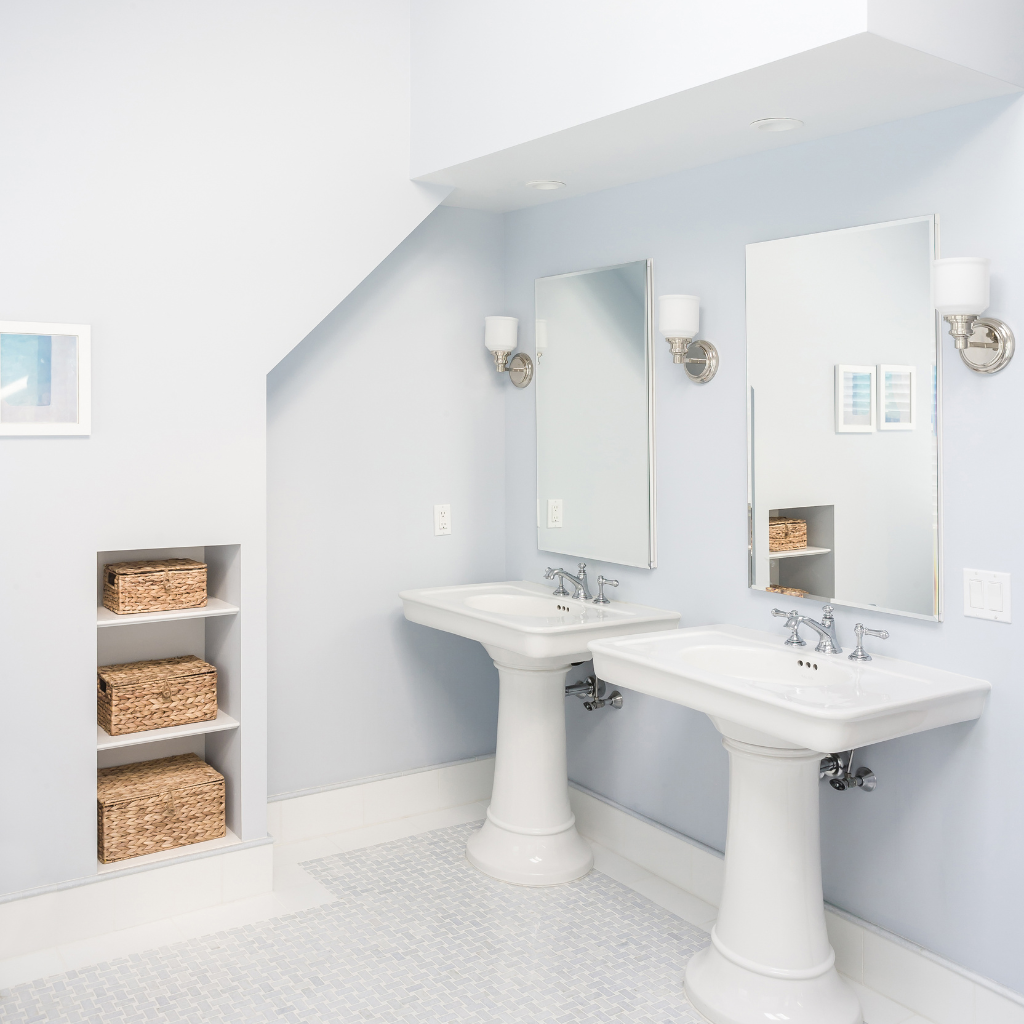 Bathroom with two white pedestal sinks, mirrors, and storage shelves.