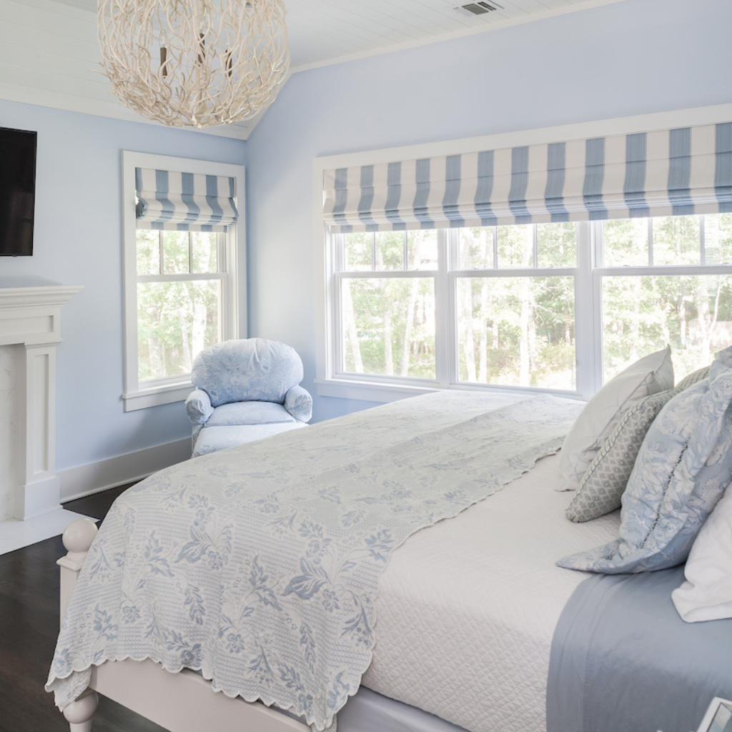 Bedroom with light blue walls, striped window shades, and a floral bedspread.
