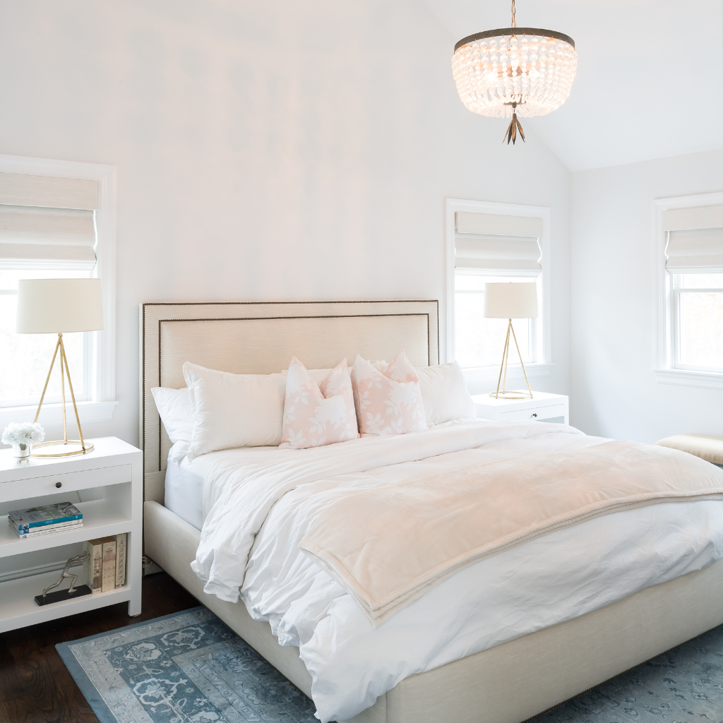 Neatly made bed in a bright bedroom with white walls and decorative lamps.