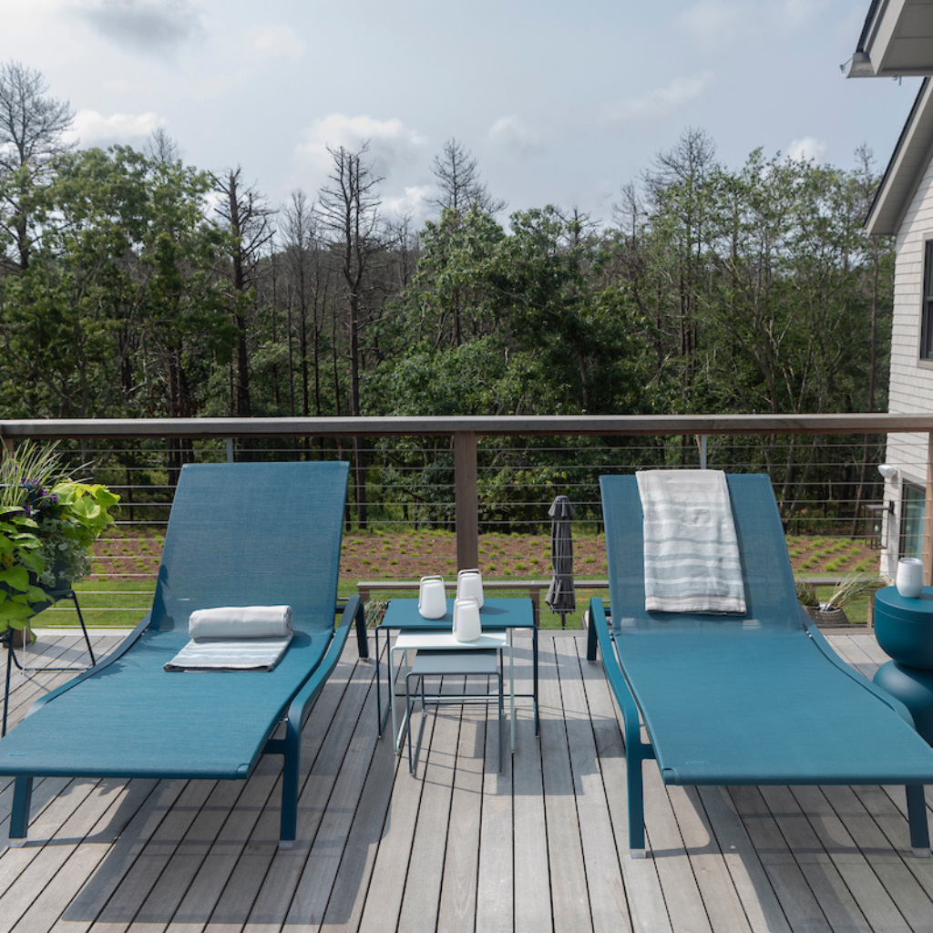 Two blue lounge chairs on a wooden deck with a view of trees and a house.