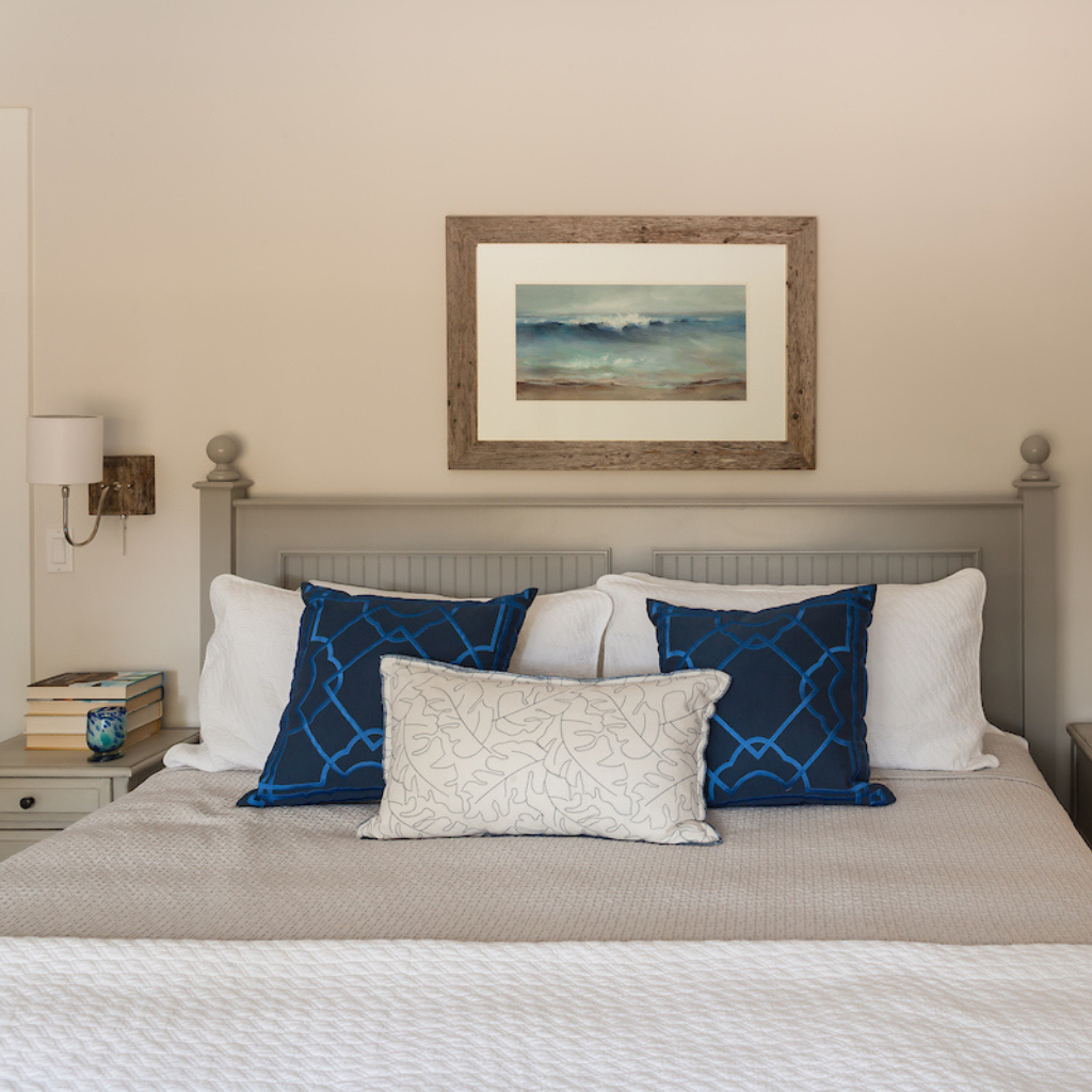 Bedroom with a bed featuring blue and white patterned pillows, a framed painting on the wall, and a nightstand with a lamp.
