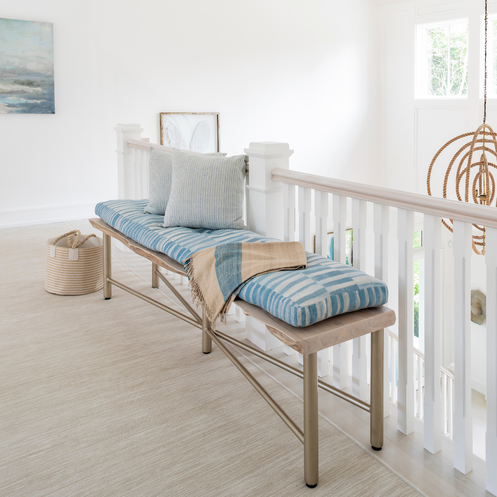 Wooden bench with blue striped cushions in a bright room with white walls and a window.