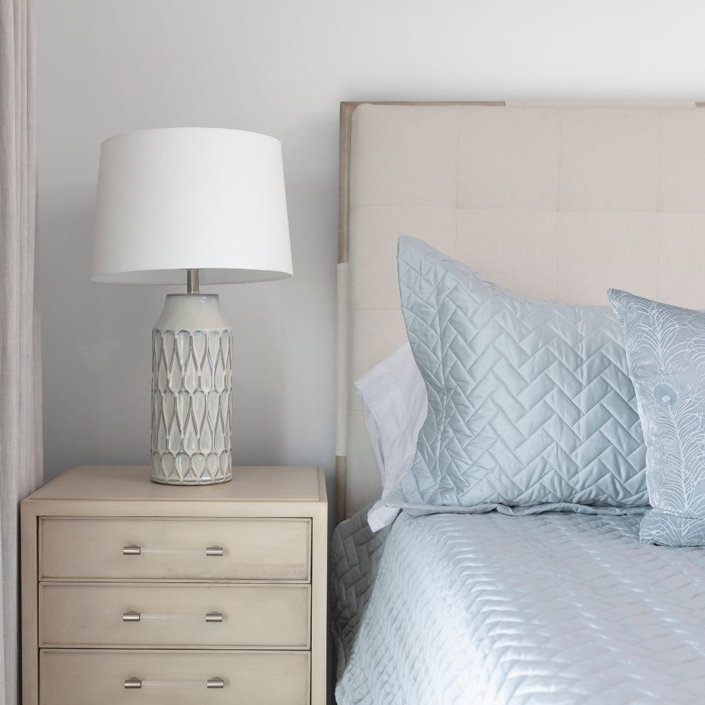 Bedroom with a bed featuring light blue bedding and pillows, next to a nightstand with a lamp.