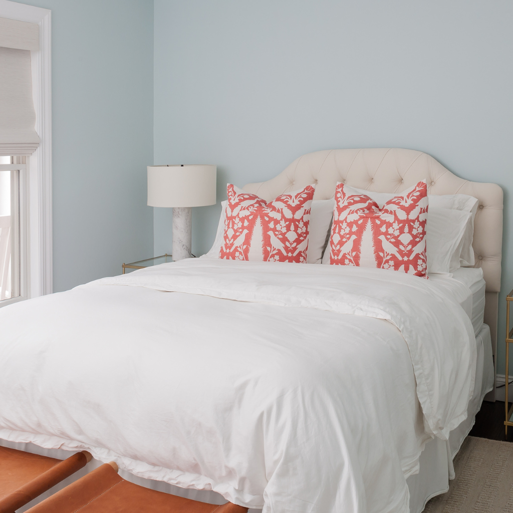 Bedroom with a bed featuring white bedding and red patterned pillows, a lamp, and light blue walls.