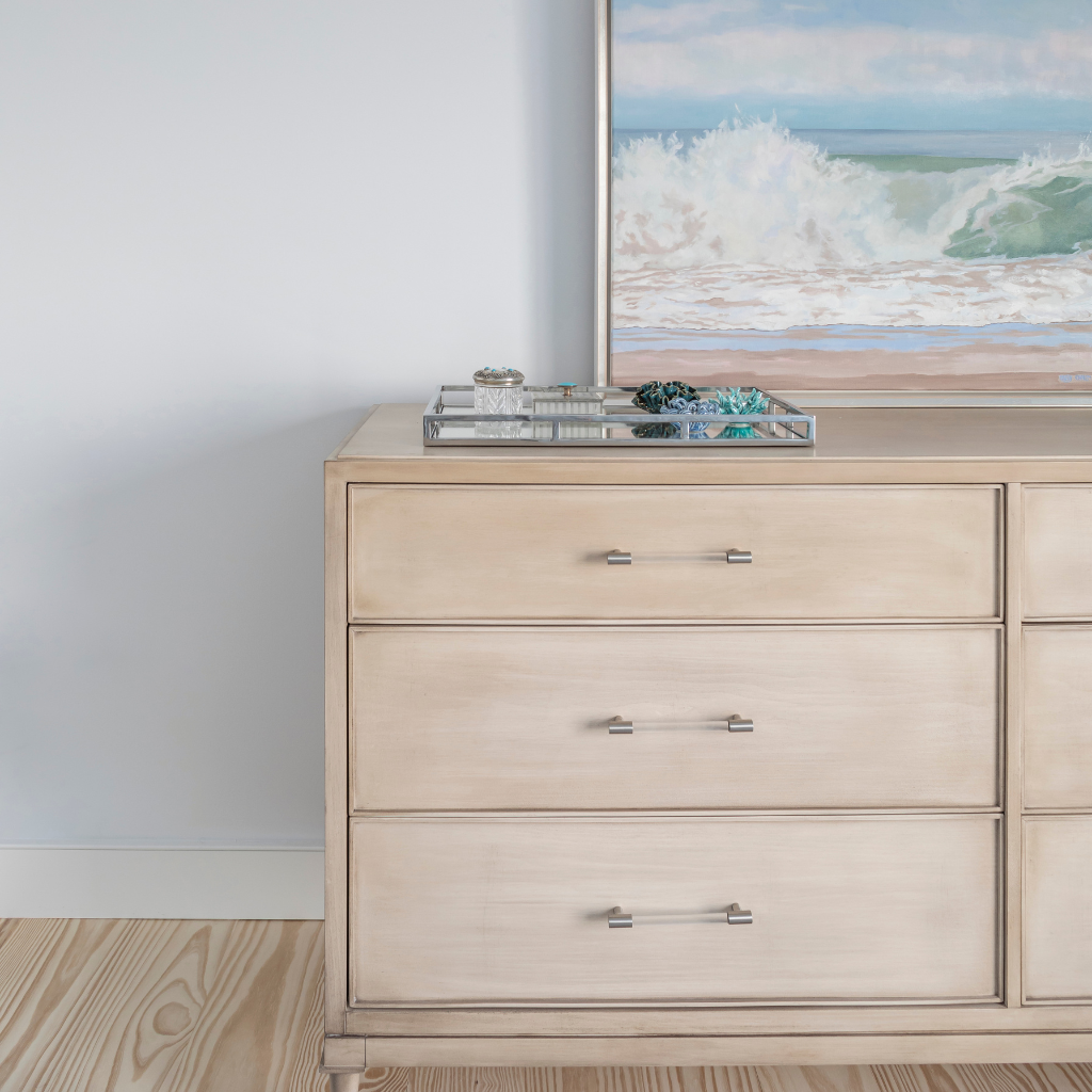 Beige dresser with metallic handles in a room with a painting of a beach scene on the wall.