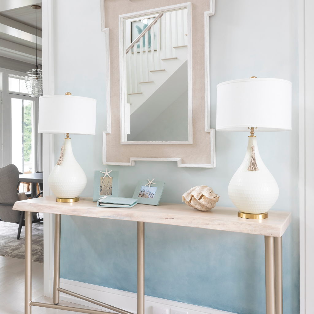 Console table with two white lamps and decorative items against a light blue wall.