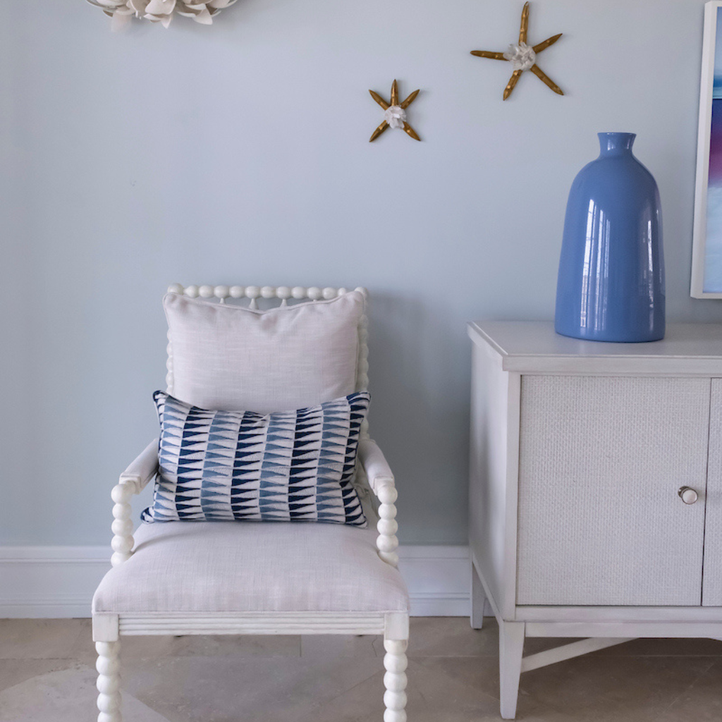 White chair with patterned pillow against a light blue wall with decorative elements.