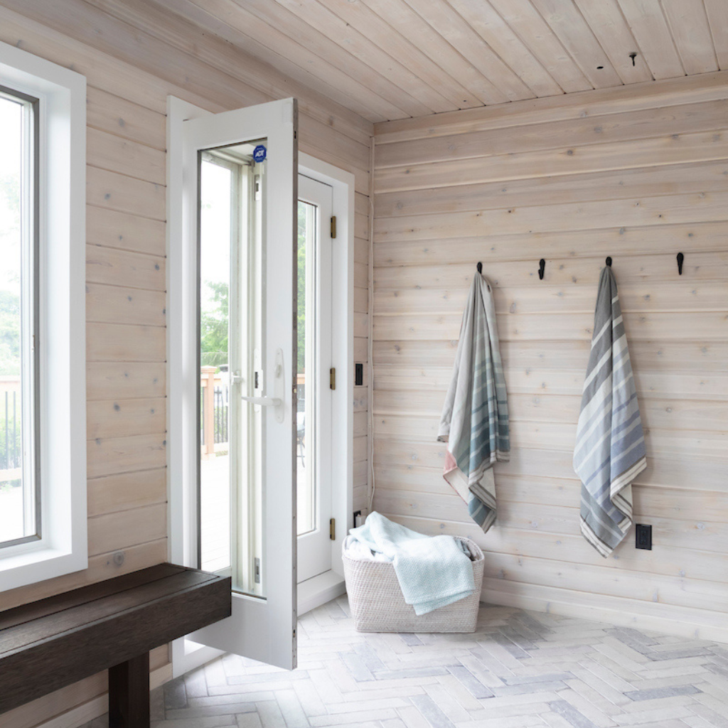 Wooden interior with towels hanging on hooks and a basket on a bench.
