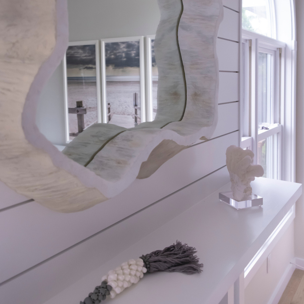 Decorative mirror on a shelf with a coastal theme, featuring a large shell and beach-themed decor.