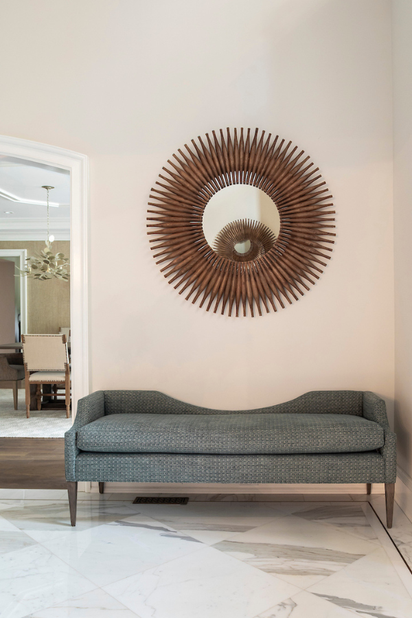 Entryway vignette with a curved upholstered bench and a large sunburst mirror, styled in warm neutral tones.