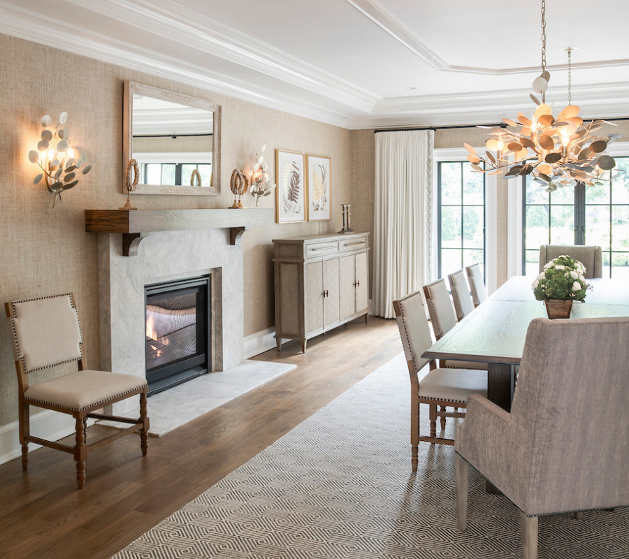 Neutral dining room with a long wood table, upholstered chairs, and a marble fireplace, accented by sculptural lighting and soft textures.