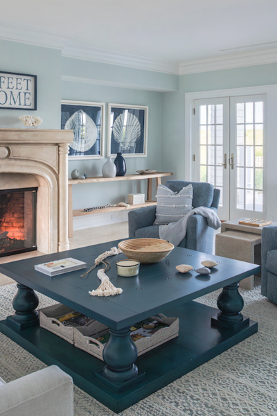 Coastal living room with a blue coffee table, upholstered seating, and a stone fireplace, styled with soft blue accents and layered textures.
