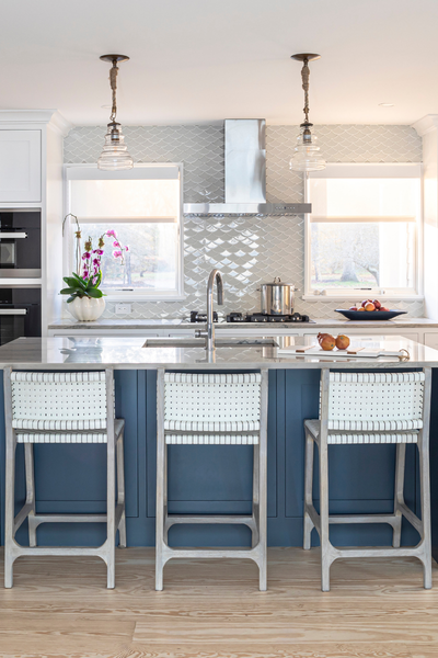 Modern kitchen with marble island and stools, featuring a backsplash and pendant lights.