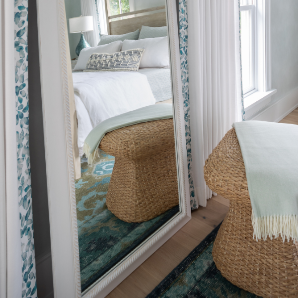 Bedroom with a large floor mirror reflecting a bed and window.