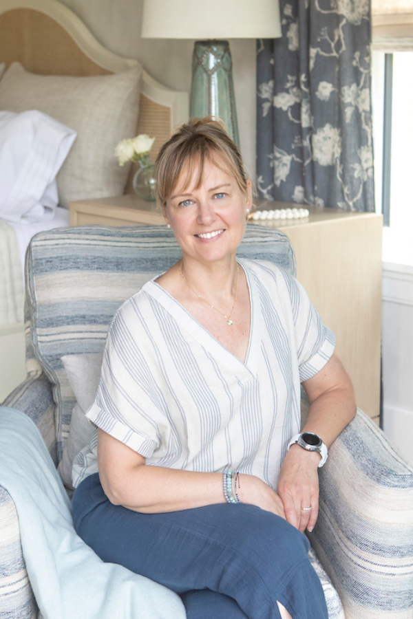Woman sitting in a chair in a room with floral curtains and a lamp.