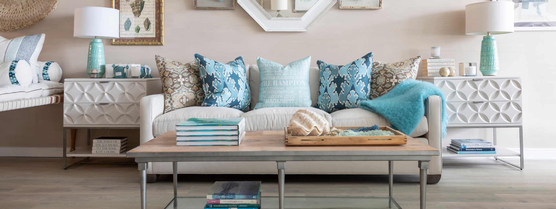 Coastal living room with a neutral sofa layered with blue patterned pillows, flanked by textured sideboards and lamps, centered around a styled coffee table.